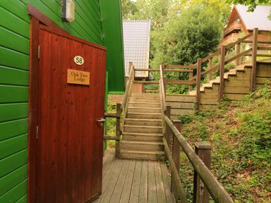 A wooden staircase with handrails leading up beside green and red wooden lodges at Oak Tree Lodge in Finlakes Holiday Park near Chudleigh