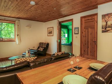 A living room with a leather sofa a glass coffee table a chaise lounge and a wooden dining table with plates and glasses at Lodge 58 - Oak Tree Lodge in Finlakes Holiday Park near Chudleigh