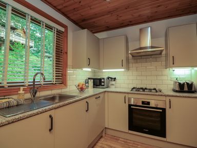 A kitchen with a sink under a window a microwave a gas stove an oven and cupboards at Lodge 58 - Oak Tree Lodge Finlakes Holiday Park near Chudleigh
