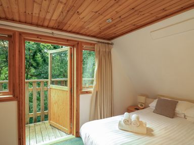 A bedroom with a double bed rolled towels bedside table lamp and open door leading to a wooden balcony at Lodge 58 - Oak Tree Lodge Finlakes Holiday Park near Chudleigh