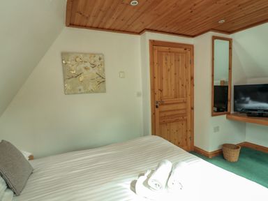 A bedroom with a bed, wooden door, wall-mounted mirror, television, basket, and floral wall art at Lodge 58 - Oak Tree Lodge Finlakes Holiday Park near Chudleigh