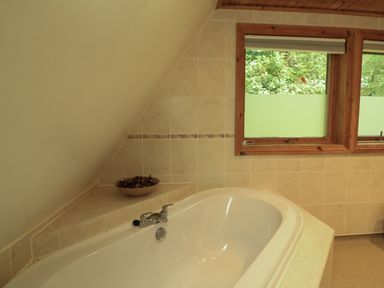 A bathroom with a white bathtub next to tiled walls and a wooden framed window at Lodge 58 - Oak Tree Lodge Finlakes Holiday Park near Chudleigh