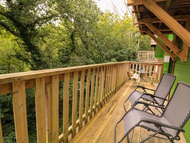 A wooden balcony with two lounge chairs and a small table with two chairs surrounded by trees at Lodge 58 - Oak Tree Lodge Finlakes Holiday Park near Chudleigh