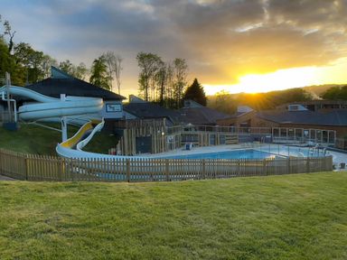 An outdoor swimming pool with a water slide and wooden fencing at sunset at Lodge 58 - Oak Tree Lodge in Finlakes Holiday Park near Chudleigh