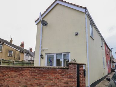 The exterior of a yellow two-story house with a brick wall and gate in front at Tiffany's Cottage in Gorleston-On-Sea