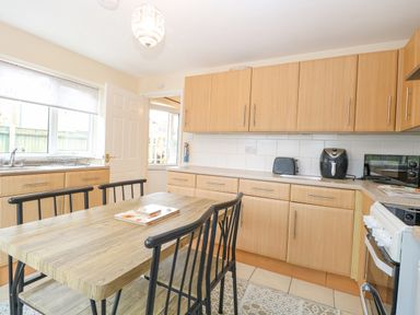 A kitchen with wooden cabinets a dining table with black chairs and appliances at Tiffany's Cottage in Gorleston-On-Sea
