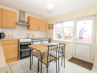 A kitchen with wooden cabinets a stove a dining table with four chairs and a door with a stained glass window at Tiffany's Cottage in Gorleston-On-Sea