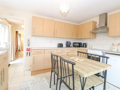 A kitchen with wooden cabinets and a dining table with black chairs at Tiffany's Cottage in Gorleston-On-Sea