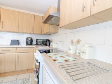 A kitchen with wooden cabinets white tiled backsplash and appliances at Tiffany's Cottage in Gorleston-On-Sea
