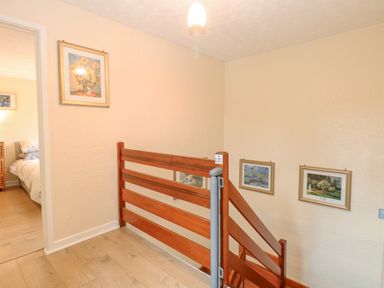 A hallway with wooden stair railing and framed pictures on walls at Tiffany's Cottage in Gorleston-On-Sea
