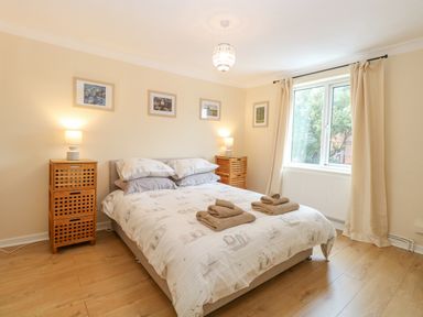 A bedroom with a double bed two wooden bedside cabinets and a window with curtains at Tiffany's Cottage in Gorleston-On-Sea
