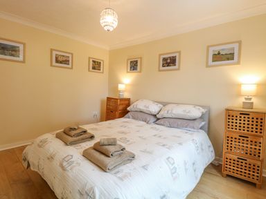 A bedroom with a bed with folded towels bedside tables with lamps and framed pictures on the walls at Tiffany's Cottage in Gorleston-On-Sea