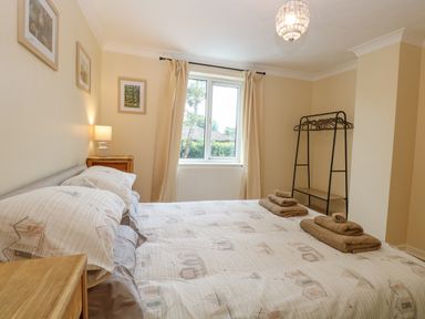 A bedroom with a double bed bedside table a lamp window with curtains and a clothes rack at Tiffany's Cottage in Gorleston-On-Sea