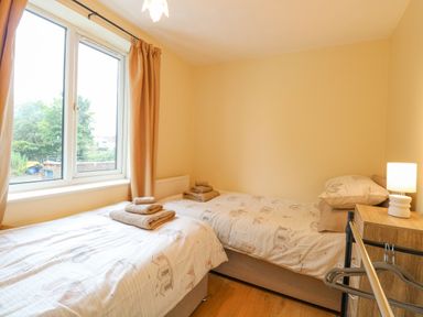 A bedroom with two single beds beige curtains and a wooden nightstand with a lamp at Tiffany's Cottage in Gorleston-On-Sea