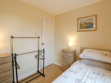 A bedroom with a bed a bedside table a lamp a clothes rack with hangers and a door at Tiffany's Cottage in Gorleston-On-Sea