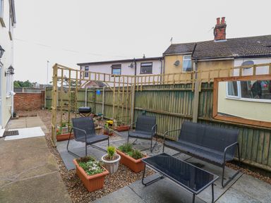 A garden area with outdoor seating furniture and potted plants surrounded by a wooden fence at Tiffany's Cottage in Gorleston-On-Sea