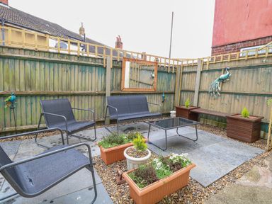 A small outdoor patio area with metal chairs a glass table planter boxes and a wooden bench at Tiffany's Cottage in Gorleston-On-Sea