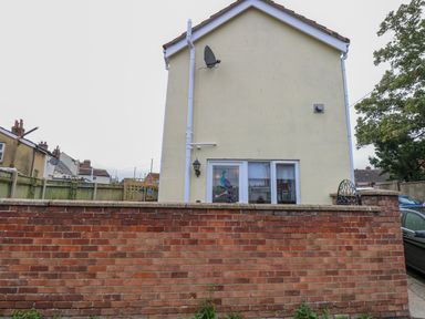 Back of a two story house with a brick wall a glass door with a stained glass peacock and a satellite dish at Tiffany's Cottage in Gorleston-On-Sea