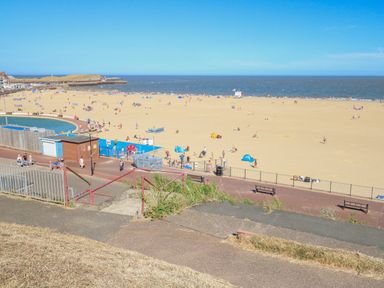 A sandy beach with people and small tents near a promenade and sea at Tiffany's Cottage in Gorleston-On-Sea