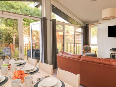 A dining area with a table set for breakfast and a living room with seating and large windows at Woodland View 7 - Oak Cabin Finlakes Holiday Park near Chudleigh