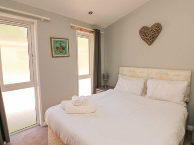 A bedroom with a double bed and rolled white towels near two windows at Woodland View 7 - Oak Cabin Finlakes Holiday Park near Chudleigh