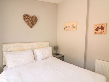 A bedroom with a double bed white pillows bedside table lamp wall art and a heart decoration at Woodland View 7 - Oak Cabin in Finlakes Holiday Park near Chudleigh