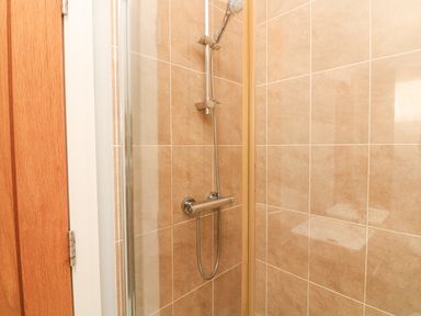A shower area with beige tiled walls a handheld showerhead and a glass door at Woodland View 7 - Oak Cabin in Finlakes Holiday Park near Chudleigh