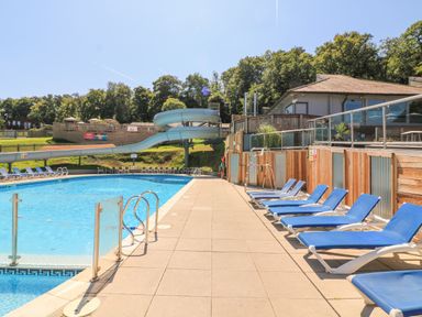 An outdoor swimming pool with a water slide and blue lounge chairs at Woodland View 7 - Oak Cabin at Finlakes Holiday Park near Chudleigh