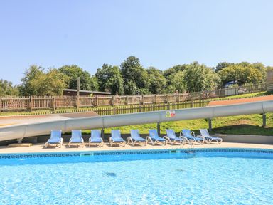 An outdoor swimming pool with blue lounge chairs and a water slide at Woodland View 7 - Oak Cabin Finlakes Holiday Park near Chudleigh