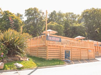 An outdoor wooden deck area with umbrellas and a sign for The Hub Shop at Finlakes Holiday Park near Chudleigh