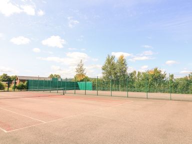 An outdoor tennis court with a net and green fencing surrounded by trees and a building at Woodland View 7 - Oak Cabin Finlakes Holiday Park near Chudleigh
