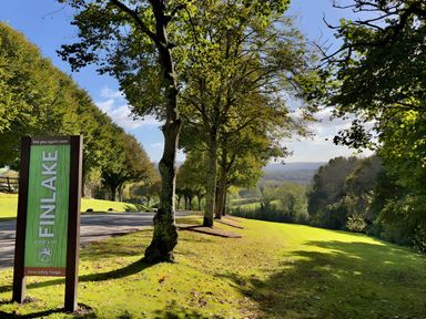 A roadside area with trees and a green sign that reads Finlake at Finlakes Holiday Park near Chudleigh