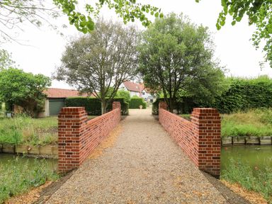 A bridge leading to a house with trees and a garden at Clock Tower in Stowmarket