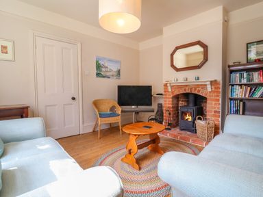 A living room with a fireplace a round wooden coffee table a television and bookshelves at Samphire House in Southwold