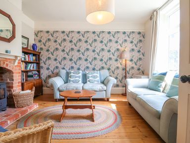 A living room with two sofas a wooden coffee table a bookshelf and a fireplace at Samphire House in Southwold