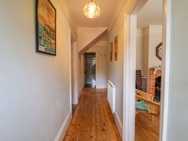A hallway with wooden floor and a radiator with a view into a room with wicker chairs and a fireplace at Samphire House in Southwold