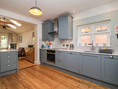 A kitchen with blue cabinets wooden floor and a window above the sink at Samphire House in Southwold