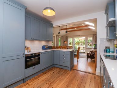A kitchen with blue cabinets and wooden floor opening to a dining area with wooden chairs at Samphire House in Southwold