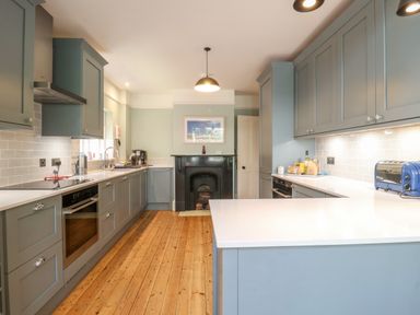 A kitchen with blue cabinets white countertops and wooden floor at Samphire House in Southwold