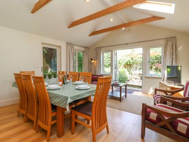 A dining room with wooden chairs and table set with plates and glasses next to a seating area and glass doors leading to a garden at Samphire House in Southwold