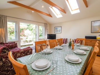 A dining room with a table set with plates glasses and cutlery next to a sitting area with armchairs and doors leading to a garden at Samphire House Southwold