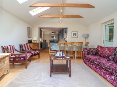 A living and dining area with wooden chairs a sofa and a kitchen at Samphire House Southwold