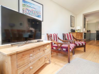A living area with a television on a wooden sideboard and two wooden armchairs with red and white striped cushions at Samphire House in Southwold