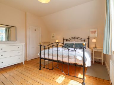 A bedroom with a black metal bed frame white dresser two bedside tables with lamps and a window with curtains at Samphire House Southwold