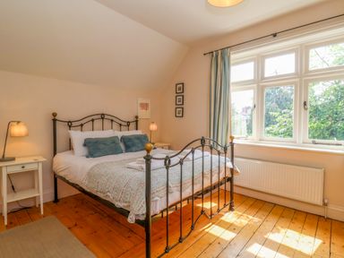 A bedroom with a metal bed frame wood floor bedside tables with lamps and a window with curtains at Samphire House Southwold