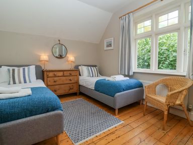 A bedroom with two single beds a wooden dresser a round mirror and a wicker chair at Samphire House in Southwold