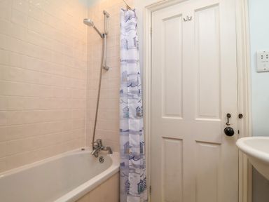 A bathroom with a bathtub shower and a door with a hook at Samphire House in Southwold