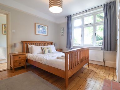 A bedroom with a wooden bed and bedside tables under a window with blue curtains at Samphire House in Southwold