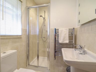A bathroom with a shower cubicle toilet sink window and towel rack at Samphire House in Southwold