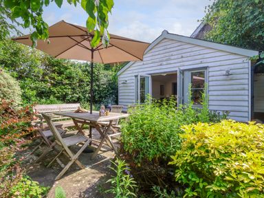 A garden patio with a wooden table and chairs under a large umbrella and plants around at Samphire House in Southwold